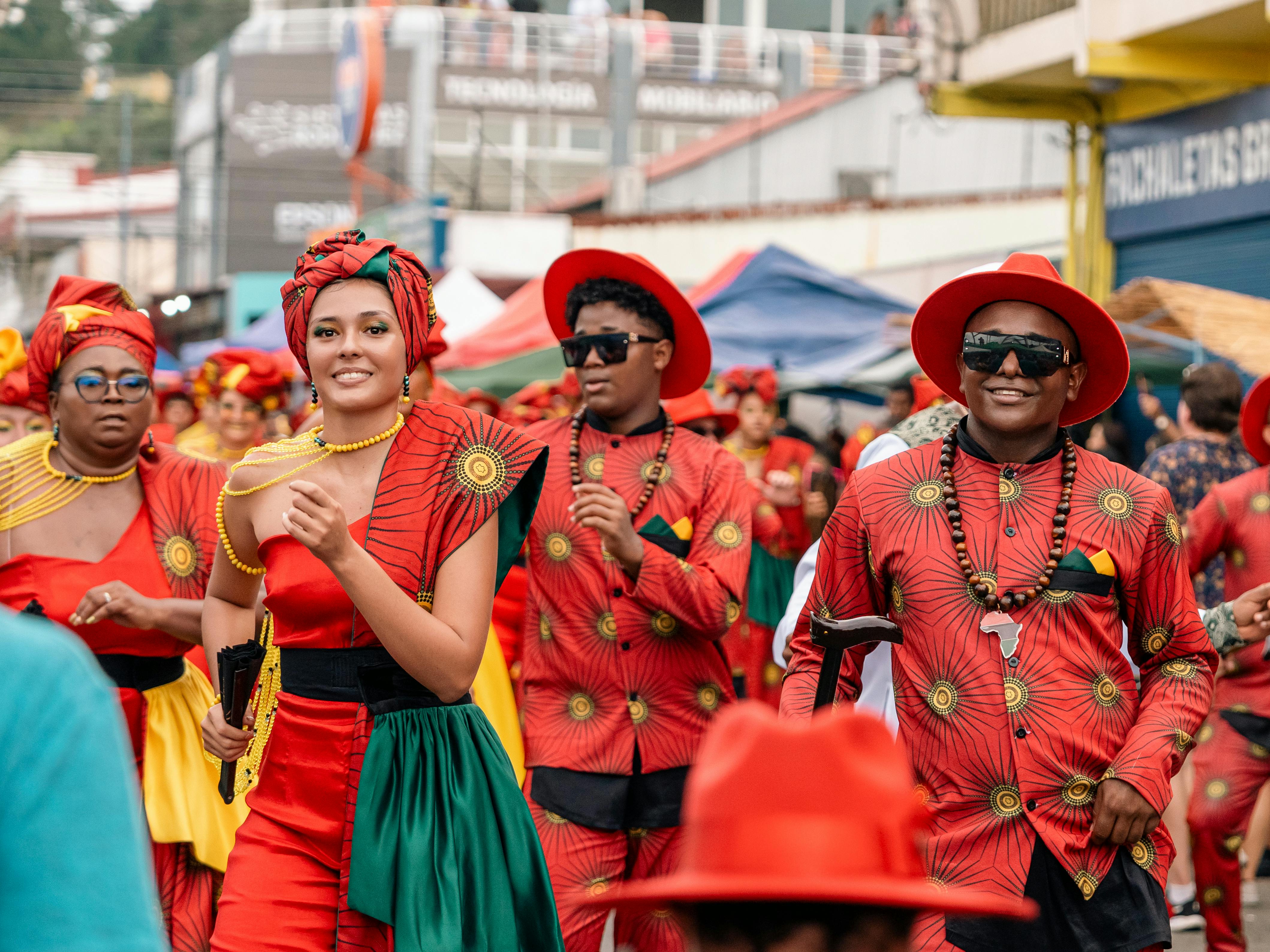 Group of people in red patterned outfits and red hats celebrating at a street carnival