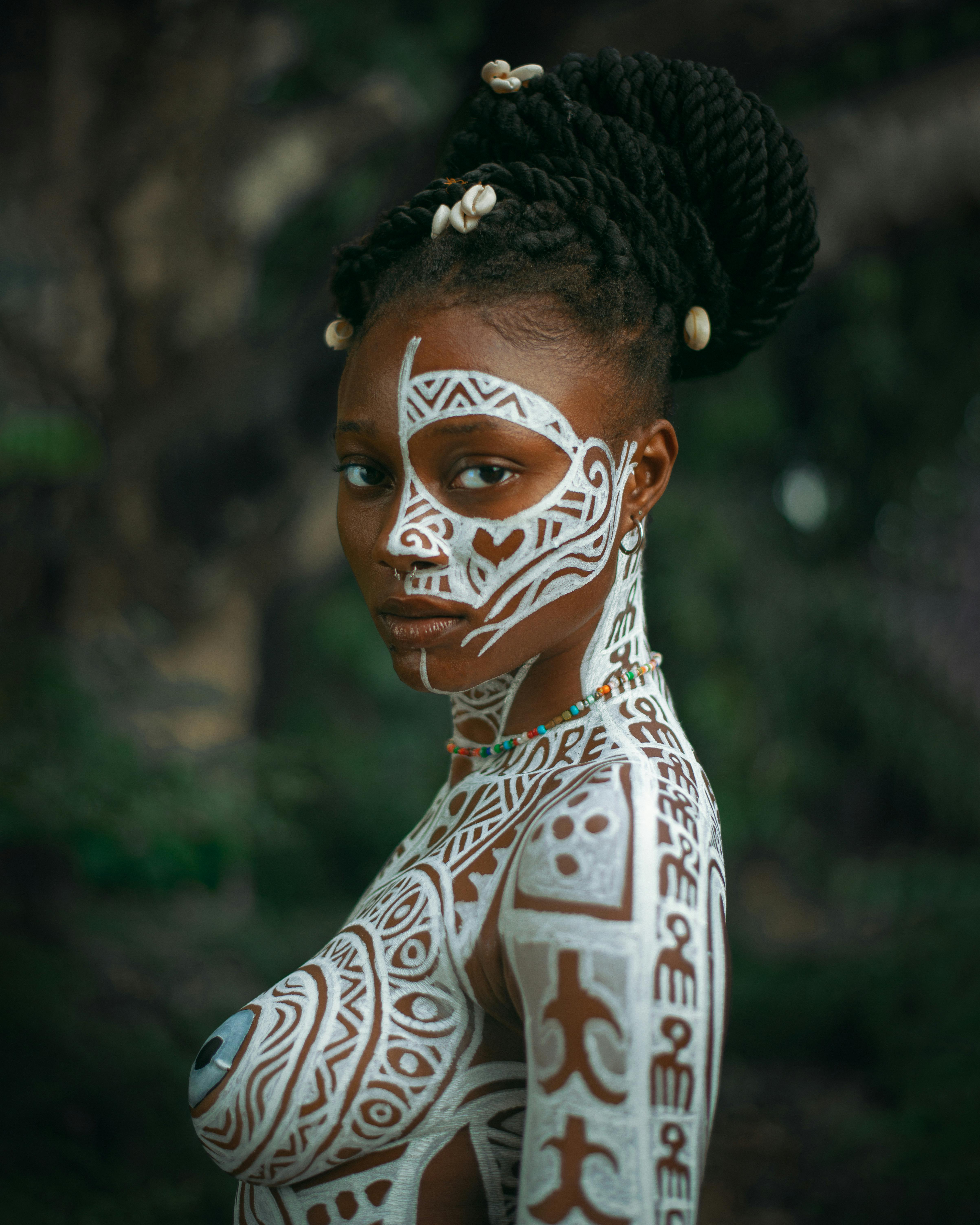 Dukka Magazine hero portrait of a woman with white tribal-style face and body paint and braided hair