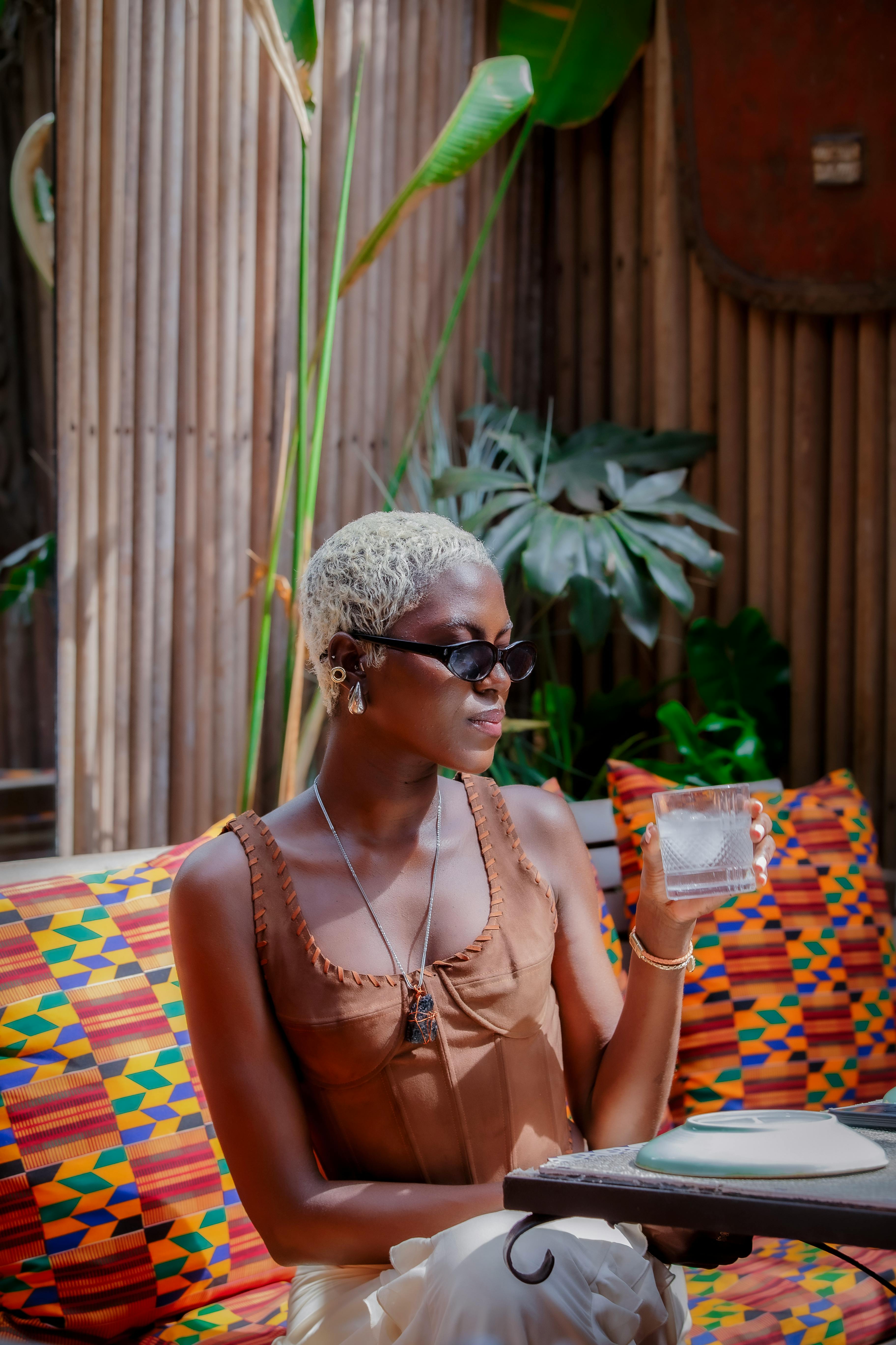 Woman in sunglasses holding a glass at a cafe table among colourful patterned cushions