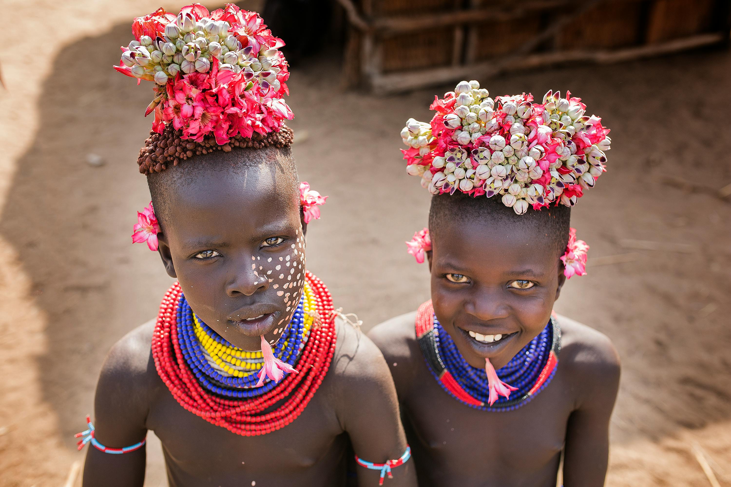 Two smiling children wearing flower headdresses and bright beaded necklaces