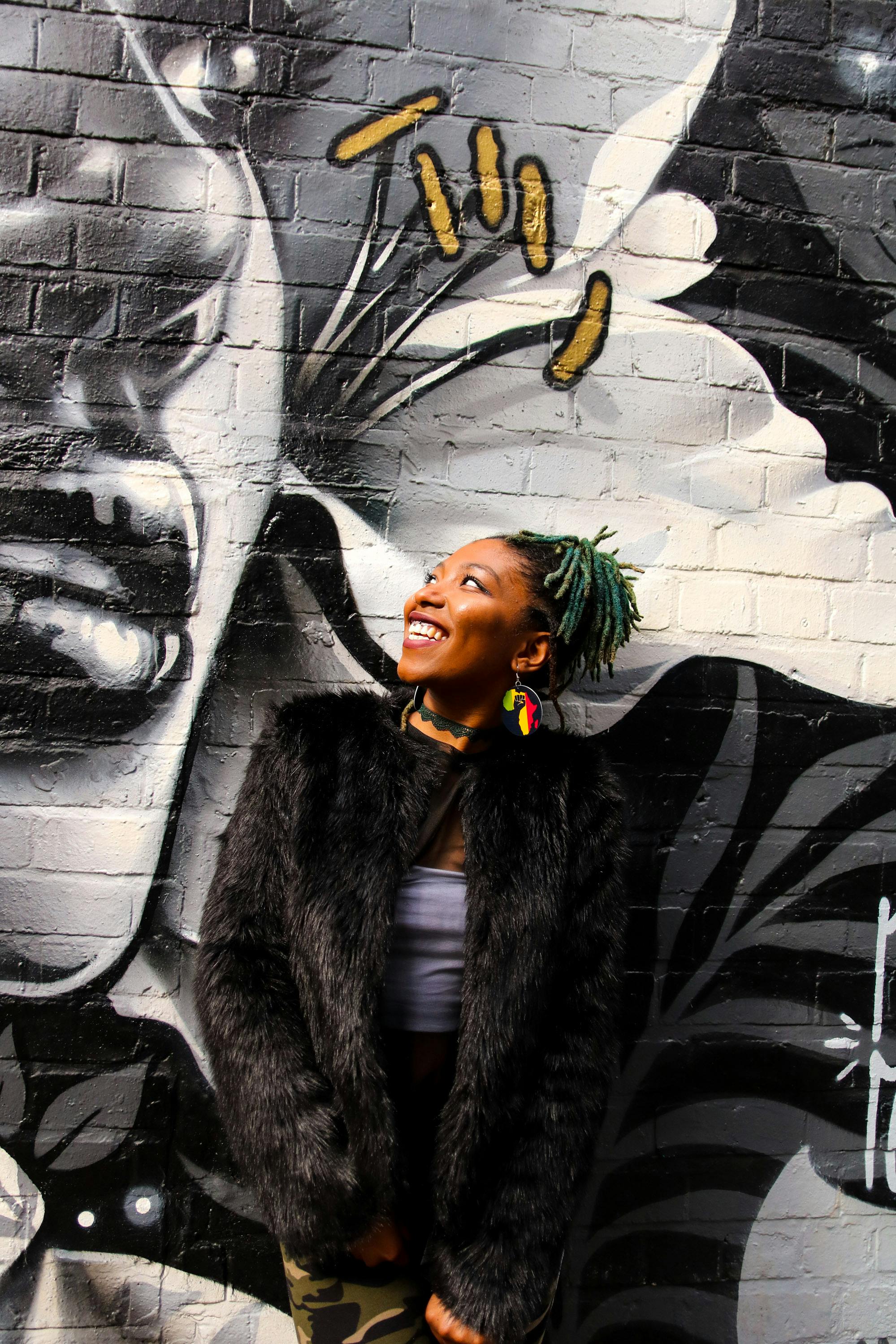 Smiling woman in a black fur jacket looking up in front of a black and white wall mural